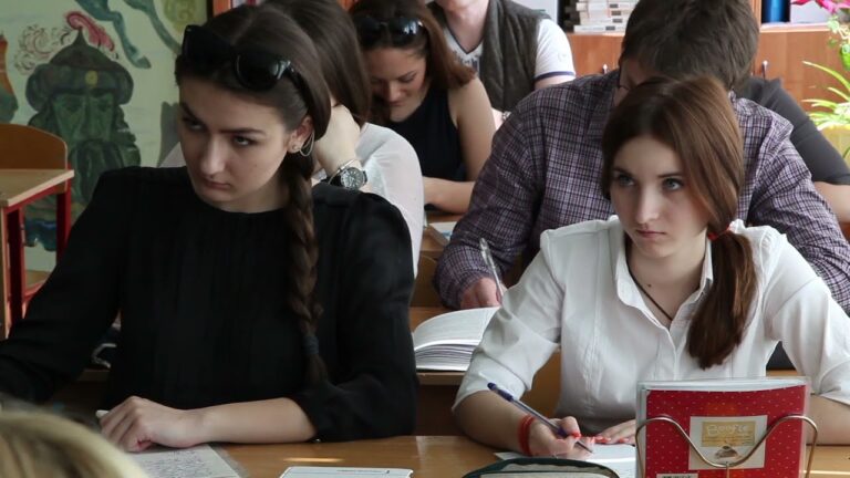 Ученицы за партой, готовятся к Дню учителя, рядом открытая книга.